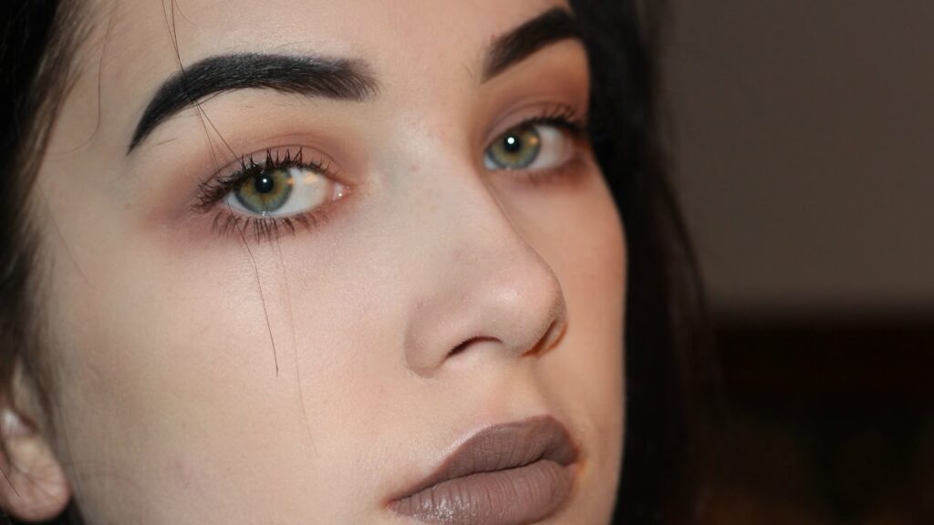 Close-up of a 90s grunge makeup look with matte brown lipstick, soft smokey eyes, and natural pale skin.